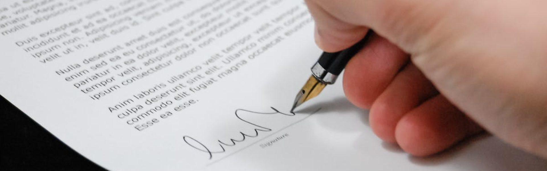 Close-up of a hand signing a legal document with a fountain pen, symbolizing signature and agreement.